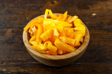 Sliced raw yellow peppers in a bowl on a wooden background. Vegetable, ingredient and staple food.
