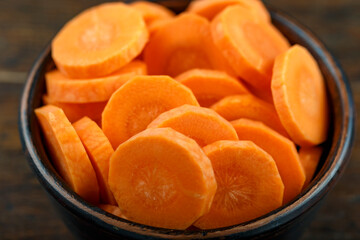 Sliced carrots in a bowl on a wooden background. Vegetable, ingredient and staple food.