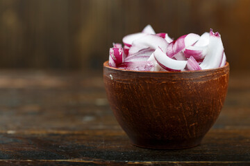 Sliced raw red onion in a bowl on a wooden background. Vegetable, ingredient and staple food.