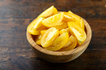 Sliced yellow tomato in a bowl on a wooden background. Vegetable, ingredient and staple food.