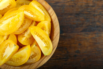 Sliced yellow tomato in a bowl on a wooden background. Vegetable, ingredient and staple food.