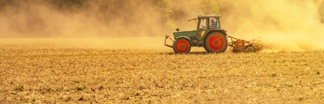 Sommer auf dem Land / Landwirtschaft Ernte Hintergrund Banner Panorama: Alter Traktor beim Fr&auml;sen von Stroh Getreide Gersten Weizen Feld, mit aufgewirbeltem Staub, im Schwarzwald, Deutschland