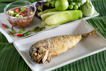 Fried mackerel in white dish and Thai Shrimp paste chili sauce (thai called  Nam Prik Kapi ) with fresh vegetables on green banana leaf