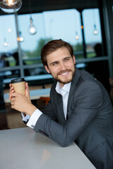 Naklejka na ściany i meble Charming young bearded businessman smiling, holding a paper cup of coffee