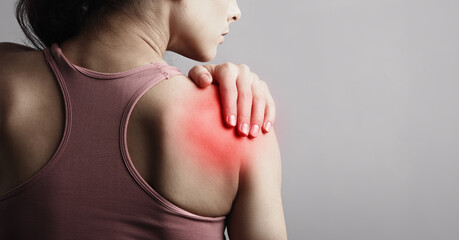 Young strong sporty woman suffering from pain in shoulder in sport wear. Touching the hand. Sports exercising injury. Closeup portrait with highlighted in red and empty space. Back view. The concept