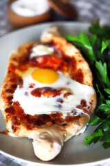 Selective focus. Macro. Khachapuri with egg and herbs on a plate.
