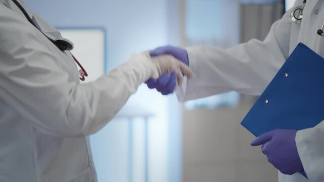 Close up of two doctors in protective gloves shaking hands after working together in hospital