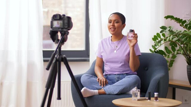 blogging, videoblog and people concept - happy smiling african american female beauty blogger with camera and perfume videoblogging at home