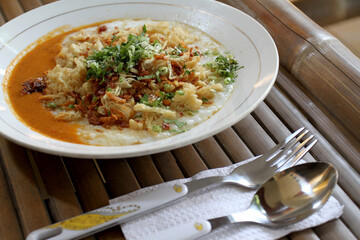 Bubur ayam or chicken porridge, Indonesian rice porridge with shredded chicken and chunks of cakwe. Breakfast dish of rice porridge with chicken, Chinese croissant, celery, and fried shallot. 