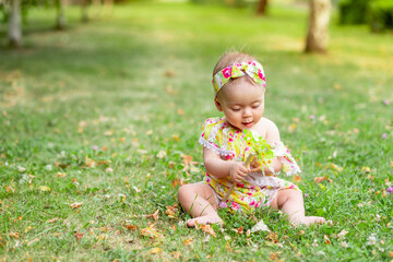 little baby girl 7 months old sitting on a green lawn in a yellow dress and playing with a toy, walking in the fresh air, space for text