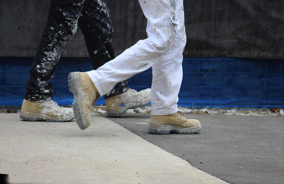 The Legs Of Two Painters Walking On A Australian Construction Site.  Their Clothing A Work Boots Are Stained.