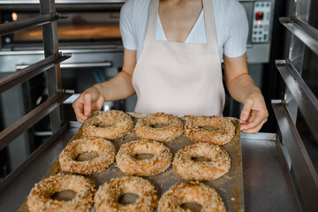 Close up baker is holding a tray with fresh bagels at baking manufacturer factory.