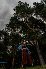 Obraz na płótnie Canvas Young woman in full growth on background of pine trees and an approaching thunderstorm