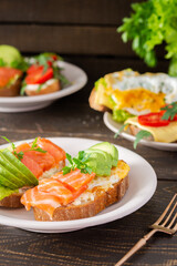 Different delicious sandwiches for breakfast, bread with cheese, avocado and trout, sandwich with egg, tomato and rucola, parsley