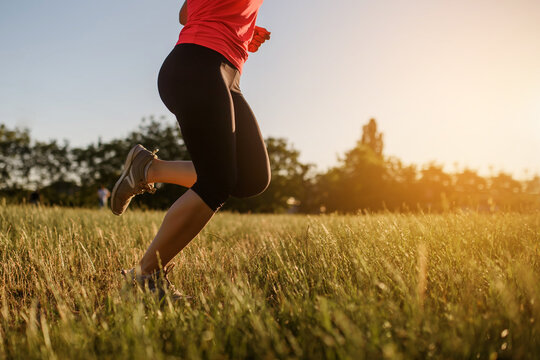Close up of a woman's legs making sport, she is running on a grass in the midst of nature on sunset.