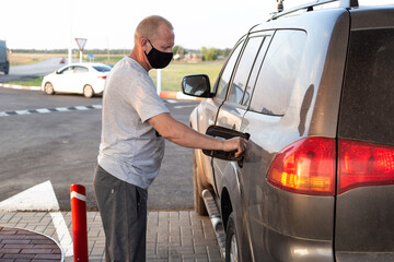 man in a black protective mask refills an SUV car at a gas station
