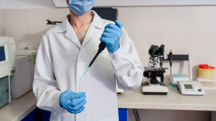 In the hospital laboratories working process, a young man doctor scientists is using micropipette test tubes near a fully-automated diagnostic chemistry system