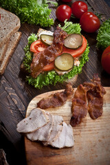 sandwich with smoked meat, green salad, fresh tomatoes and pickled cucumbers, on kitchen wooden table background