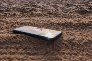 Mobile phone buried in the grey sand, lose your smartphone on the beach while on vacation.