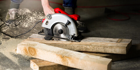 Man with circular saw for cutting boards. Construction and home renovation in the workshop. Worker saws a wooden plank at a construction sit. 
