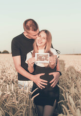 
A pregnant woman holds an ultrasound scan in her hands and a man hugs her