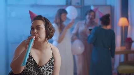 Portrait of excited plus size young girl celebrating birthday standing with hat and party whistle