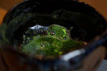 closeup of green matcha tea powder in dark ceramic bowl