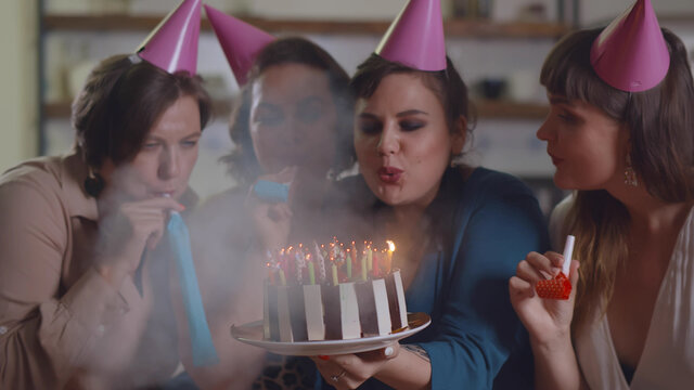 Woman blowing out candle on cake at birthday party with friends at home