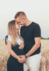 
Man kisses and hugs a pregnant woman in the field