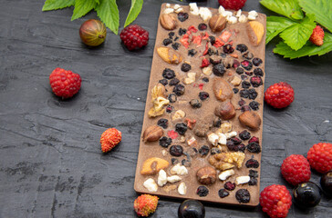 Chocolate bars, various ripe berries and mint leaves lie on a black slate background.