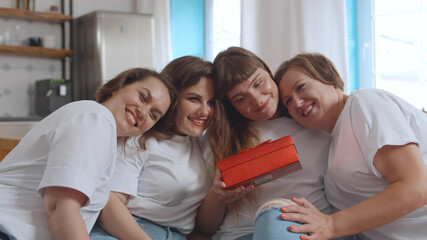 Beautiful girlfriends giving present to happy bride during party at home
