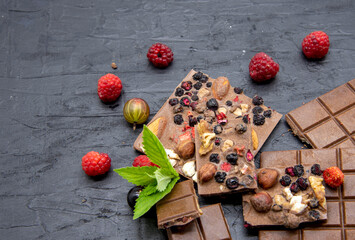 Chocolate bars, various ripe berries and mint leaves lie on a black slate background.