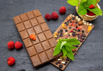 Chocolate bars, various ripe berries and mint leaves lie on a black slate background.