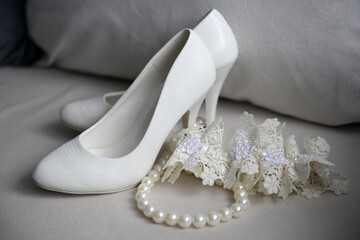 Wedding shoes of a bride near to a garter and beads close-up.