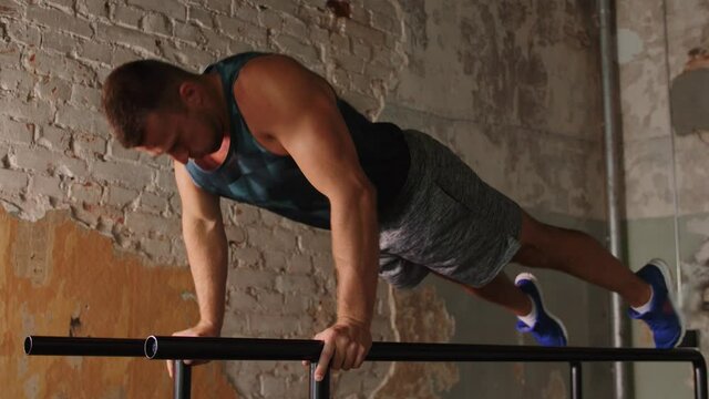 fitness, sport, bodybuilding and people concept - young man doing push-ups or high plank on parallel bars in gym