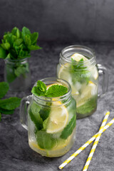 Two glasses of ice tea with fresh mint, lemon and paper straw on dark background. Summer healthy cold drink. Alternative medicine.
