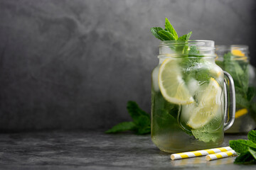 Glass mason jar of ice tea with fresh mint, lemon and paper straw on dark background. Summer healthy cold drink. Copy space.