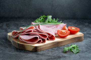 Close up ham slices isolated on cutting board with arugula over dark background.