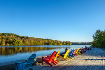 Man relaxing in a row of brightly colored adirondack chairs along waterfront in fall/autumn