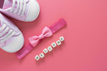 Baby girl pink background with newborn shoes, bow and Welcome words. Baby flat lay.