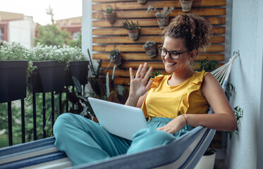 Young woman working on balcony. Young business woman using laptop computer to take video conference.