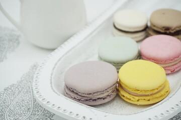 Handmade flavored French macarons on the plate, pastel colors, white milk pottery in the background, landscape frame 