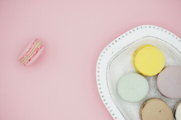 Handmade flavored French macarons on white plate on light pink background, isolated light pink macaron out of plate, portrait frame, free text, card