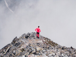 A lone traveler stands on the edge of a mountain cliff in the fog and looks into the abyss