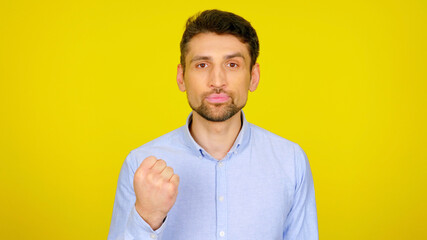 Bearded man shows fist on yellow background with copy space. Handsome guy in light blue shirt. Place for text or product