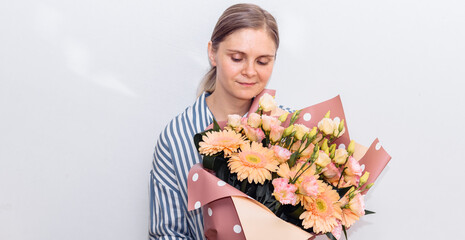young woman in a striped blue blouse holds a huge bouquet of orange gerbera rose flowers. birthday gift to the woman. 