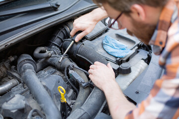 Horizontal view of a man fixing a car with a screwdriver. Self automobile repair.