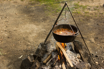 Cooking camping outdoor meal in an open fire in a travel pot with blaze. Dinner during travel.