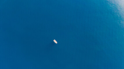 Fototapeta na wymiar Aerial view of a small boat standing still in the middle of the blue waters of Aegean sea.