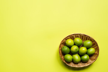 top view of ripe limes in wicker basket on colorful background